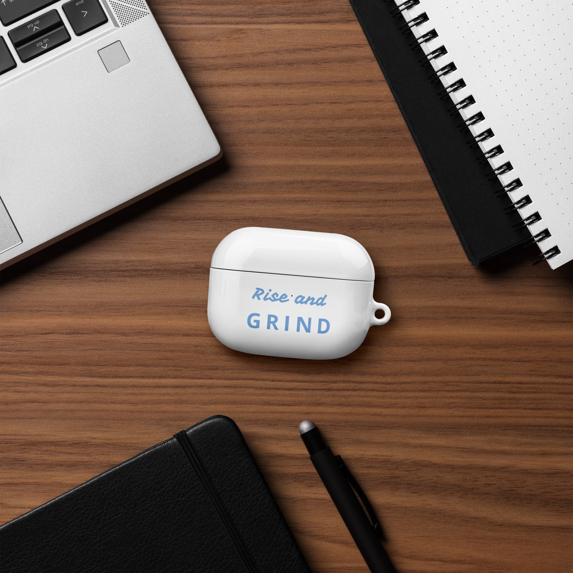Product mockupRise & GRIND Case for AirPods on a desk with laptop and notebook, showcasing stylish protection.