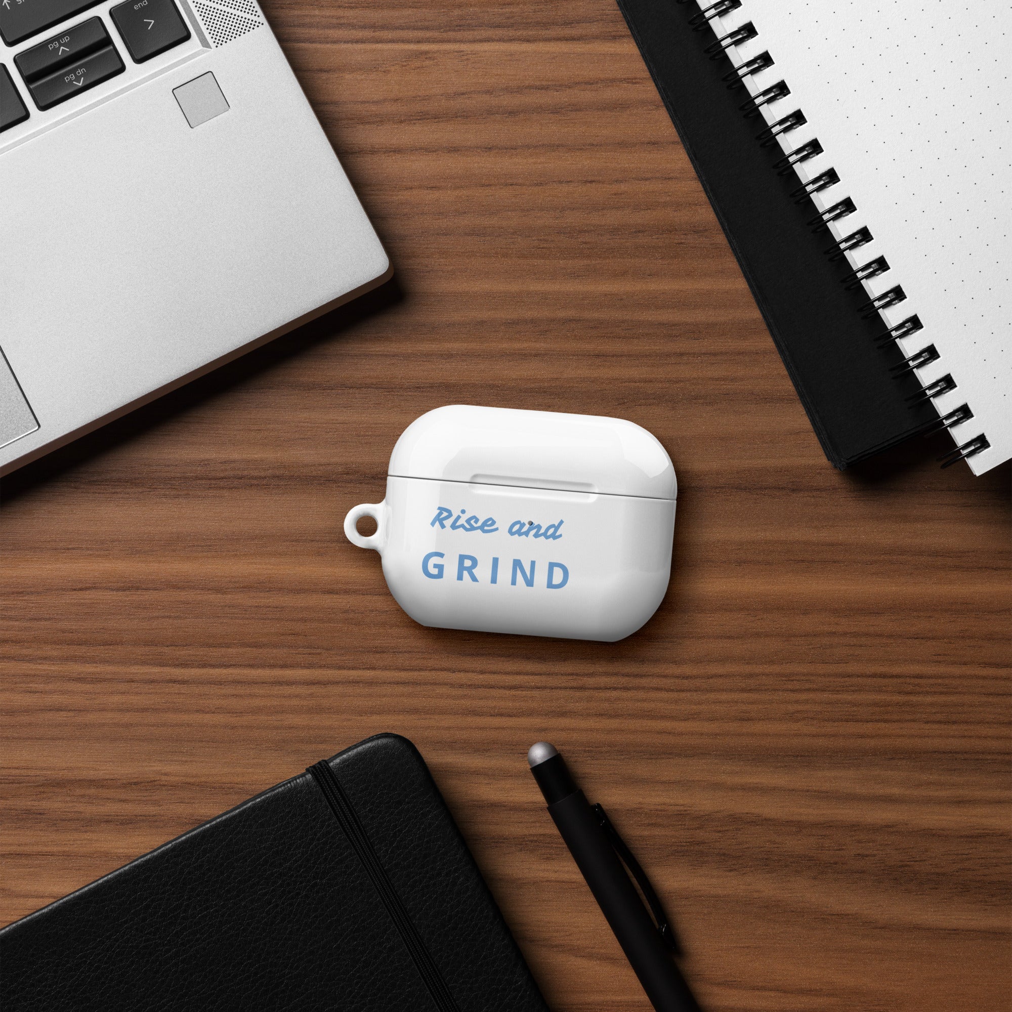Rise & GRIND Case for AirPods on a desk with laptop and notebook, showcasing stylish protection.