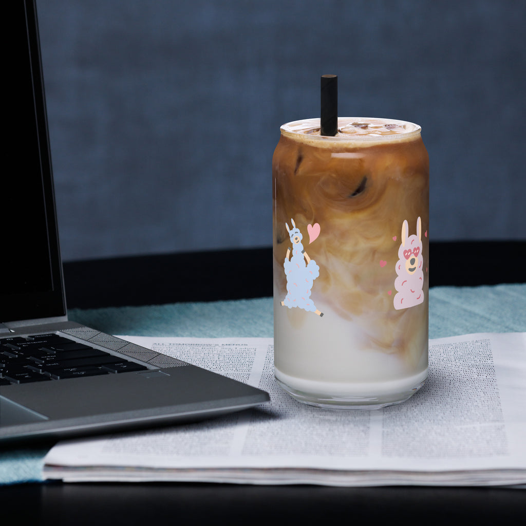 Sheep glass with straw filled with iced coffee and silver straw, placed on a table beside a laptop.