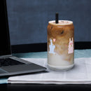 Sheep glass with straw filled with iced coffee and silver straw, placed on a table beside a laptop.