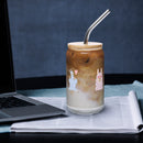 Sheep glass with straw filled with iced coffee and silver straw, placed on a table beside a laptop.