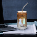 Sheep glass with straw filled with iced coffee and silver straw, placed on a table beside a laptop.