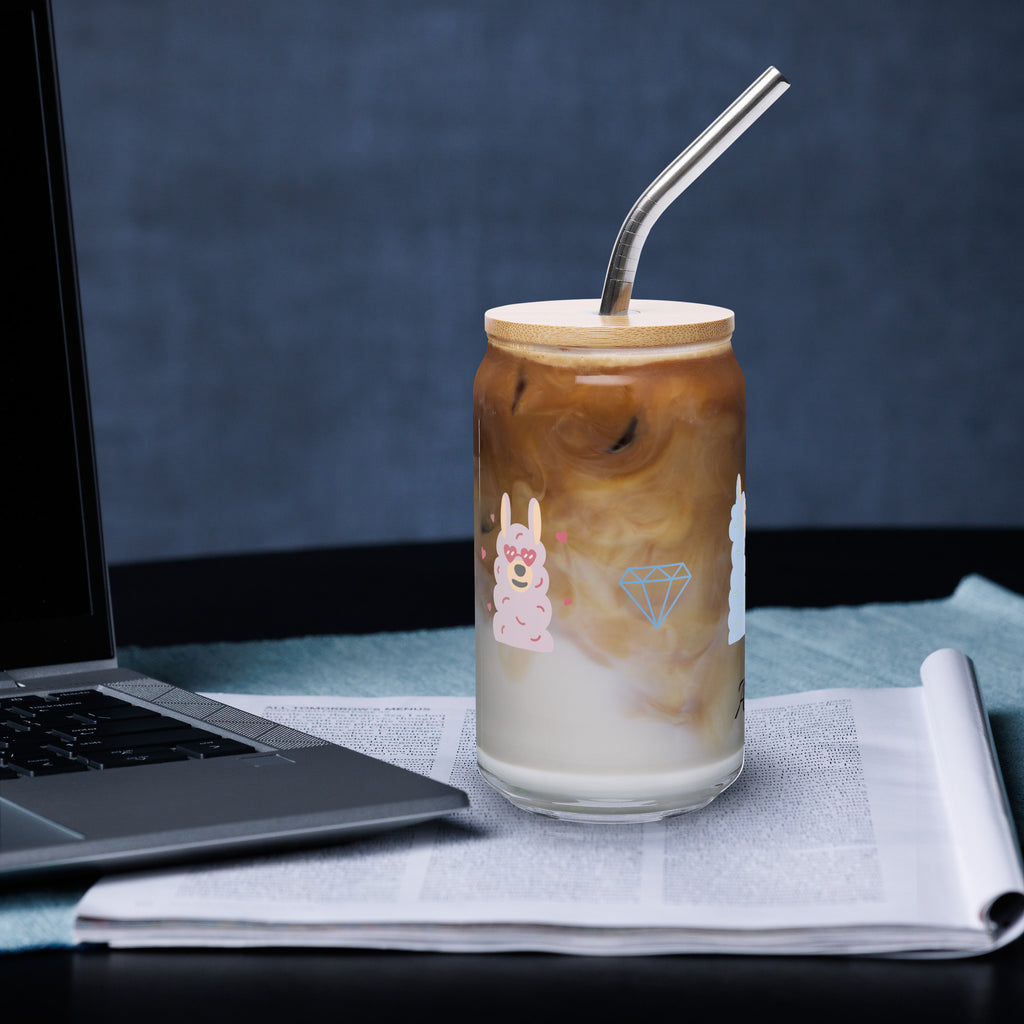 Sheep glass with straw filled with iced coffee and silver straw, placed on a table beside a laptop.